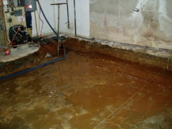 Basement excavation showing water accumulation on concrete slab, with visible plumbing and wall structure, related to A.M. Shield Waterproofing's groundwater management services.
