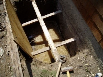 Excavated pit for basement waterproofing project, showing wooden supports and standing water, relevant to A.M. Shield Waterproofing's groundwater management services.