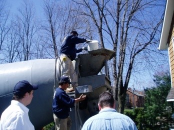 Workers operating a concrete mixer, adding materials for waterproofing, with trees and residential buildings in the background, illustrating A.M. Shield Waterproofing's concrete slab installation process.