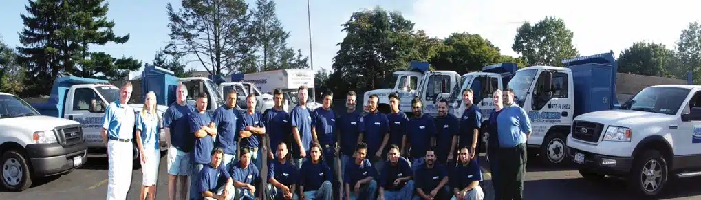 Team of A.M. Shield Waterproofing staff in blue shirts, standing in front of company trucks, showcasing expertise in basement waterproofing services.