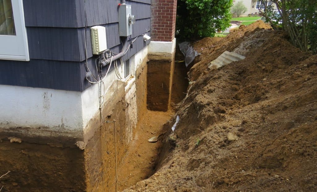 Exterior foundation waterproofing excavation showing trench along basement wall for waterproof membrane installation
