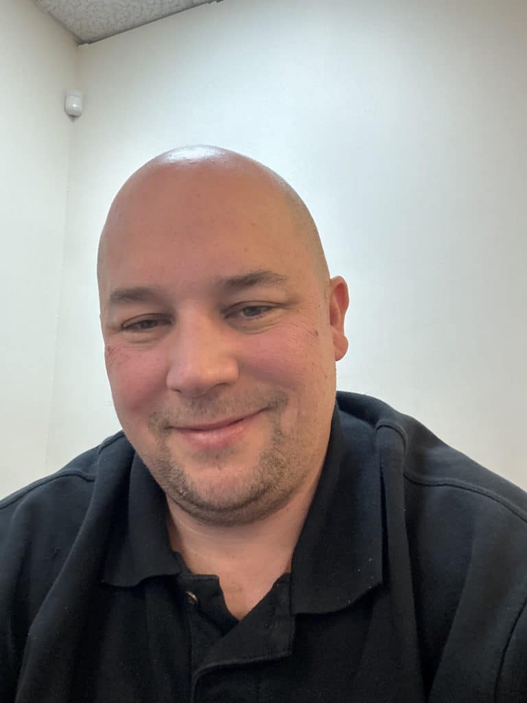 Man with a shaved head and black polo shirt smiling, representing A.M. Shield Waterproofing's team expertise in basement waterproofing solutions.