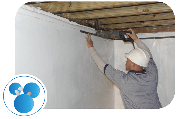 Worker installing waterproofing system in a basement with white plastic sheeting, emphasizing foundation protection against moisture intrusion.