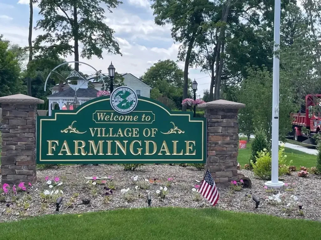 Welcome sign for the Village of Farmingdale, featuring decorative landscaping, flowers, and an American flag, symbolizing community and local pride.