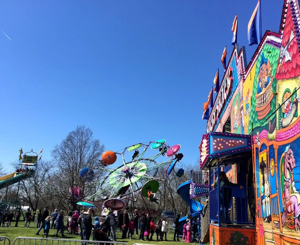 Colorful carnival rides and attractions at a festive outdoor event, with people enjoying the activities under a clear blue sky.