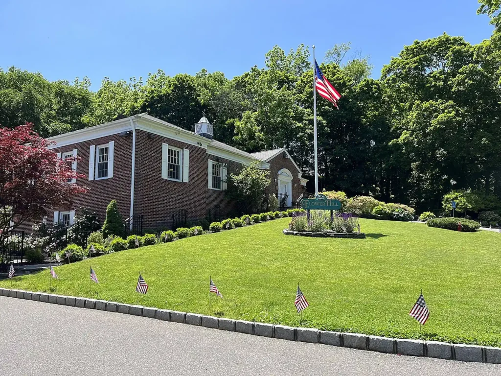 Flower Hill community center building with American flags in the front yard, surrounded by landscaped greenery, emphasizing local pride and community engagement.
