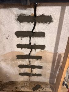 Close-up of a concrete wall repair, showing horizontal patches of fresh gray mortar covering cracks. Shadows and wooden framing create a construction site feel.